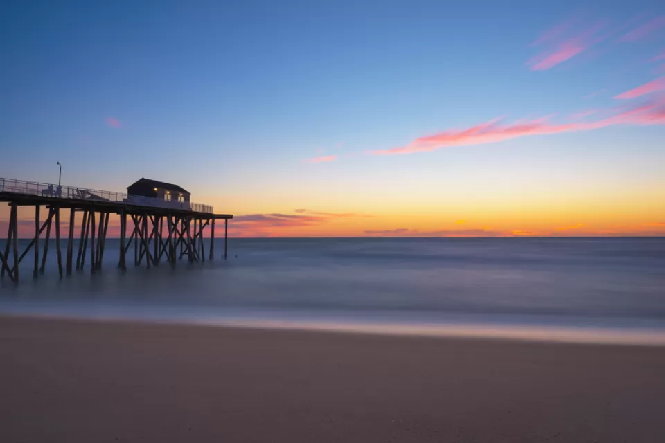 View of empty beach with wooden fishing pier going out into Atlantic Ocean at sunset in New Jersey